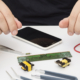 Ilustración de manos reparando dispositivo con componentes electrónicos.