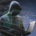 Ilustración de un hacker encapuchada escribiendo código en una laptop